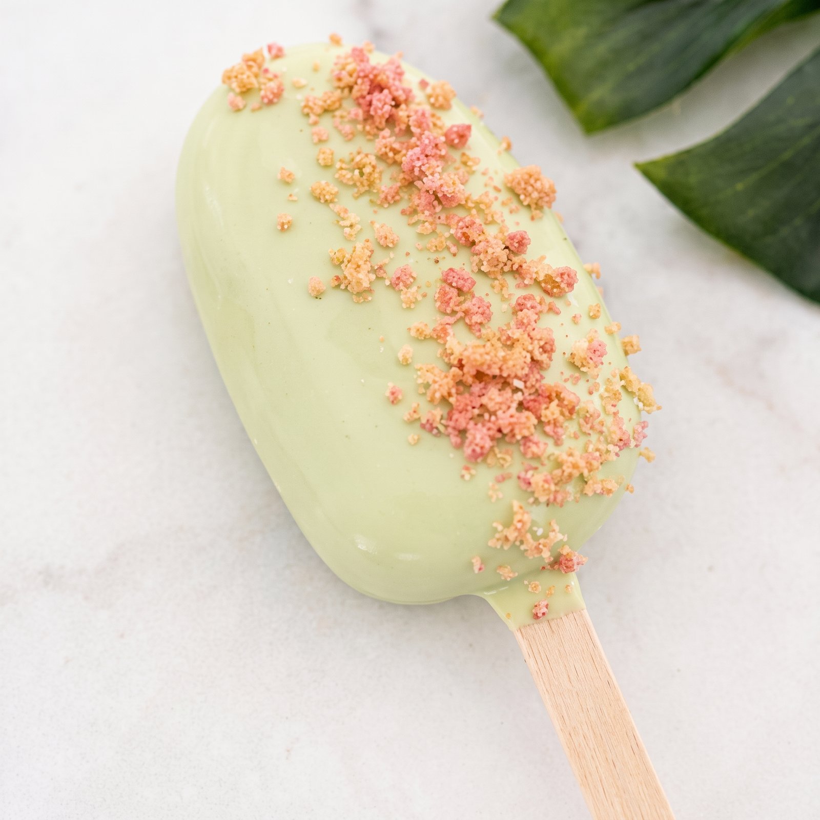 A green cakesicle topped with strawberry crunch